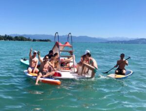 Eine Gruppe von Jugendlichen sitzt auf einem Tretboot mit Rutsche und SUPs auf dem Bodensee
