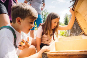 Die Kinder blicken gespannt in die Schatztruhe des Erlebniswegs Karrengold.